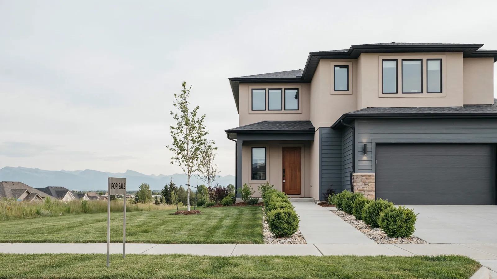 A modern two storey home with mountains behind it and a for sale sign on the lawn, the Red Deer foreclosure guide